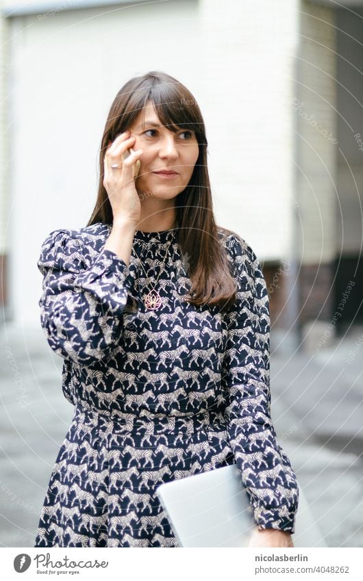 Woman talking on cell phone and has laptop in hand Communicate call Easygoing Elegant Internet urban secretary Wireless Modern job Communication Self-confident