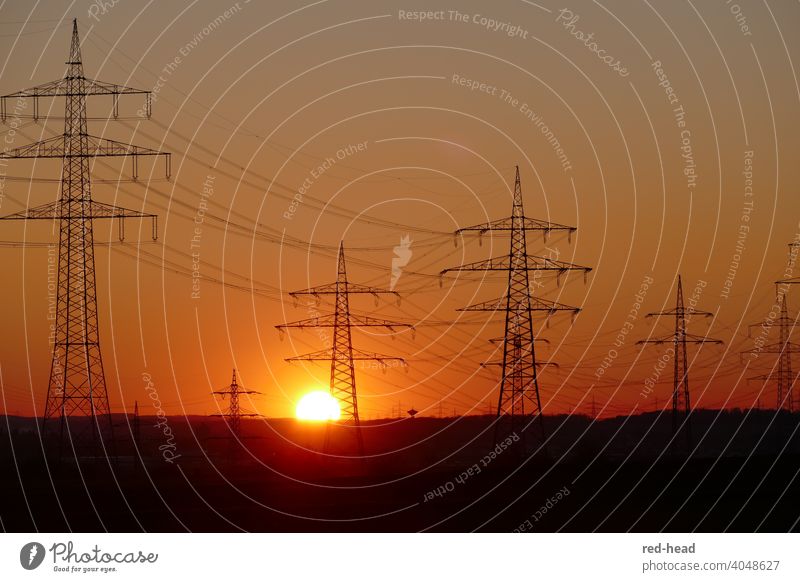 High voltage pylons in front of orange-red evening sky, sun touches horizon behind power pylon Stromm Energy Sunset power line High voltage power line