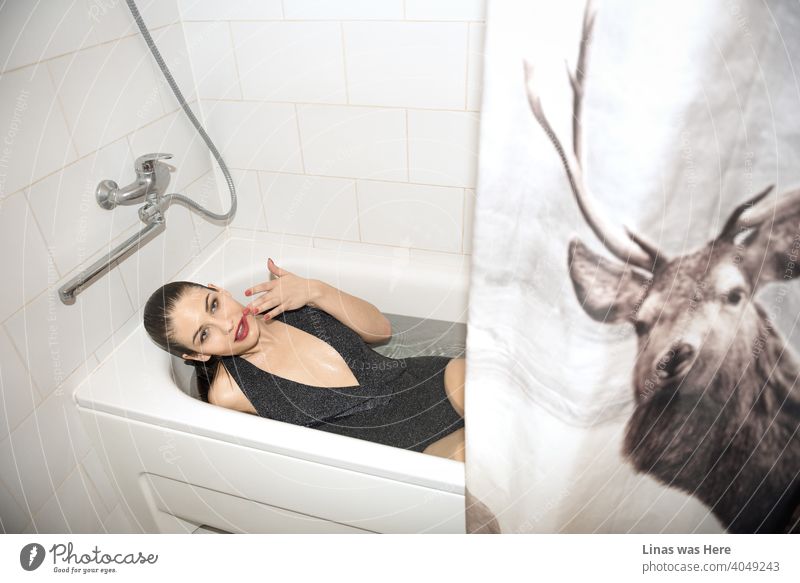 A gorgeous brunette model is taking a bath dressed in a shiny body. A sensual image of this sexy woman. Some other details like deer curtains and her red lips are visible also. Her red nails touch her beautiful face.