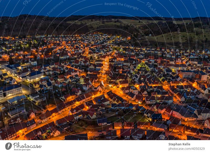 Aerial view over an illuminated city with cars at the streets and orange lights of lanterns and a hill behind the little town. night aerial urban background