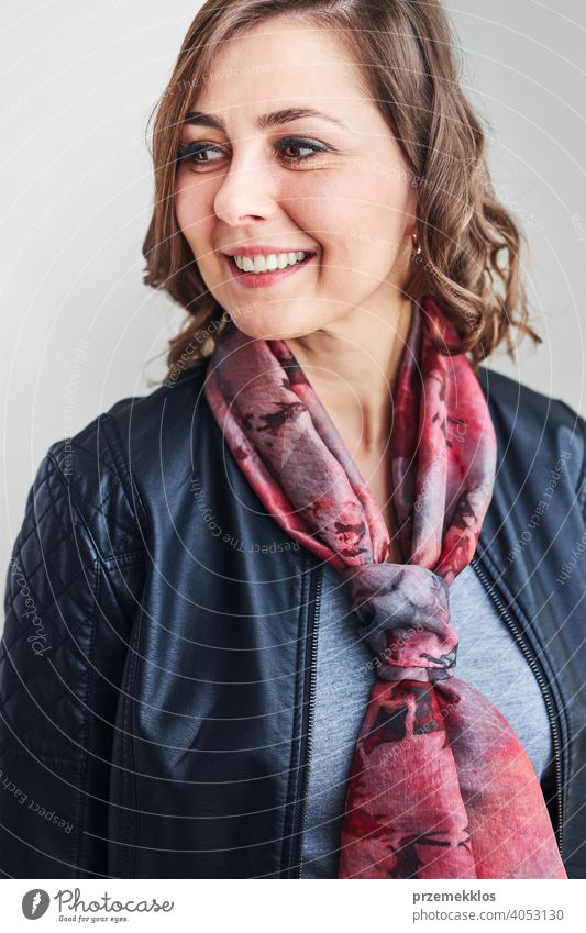 Young beautiful smiling woman wearing silk scarf around her neck and leather jacket looking away standing at plain background person model portrait beauty style