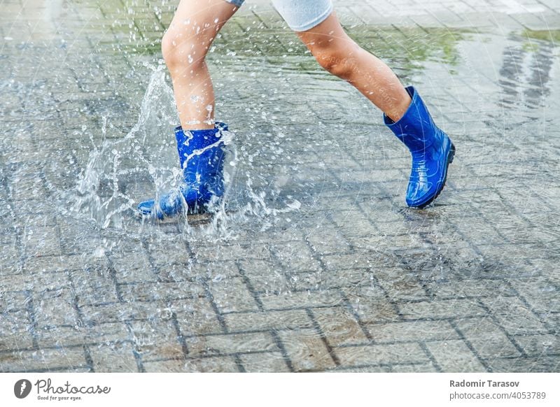 girl in blue rubber boots jumping in a puddle after a rain autumn water season wet weather walk fun child outdoors legs street nature young wearing people