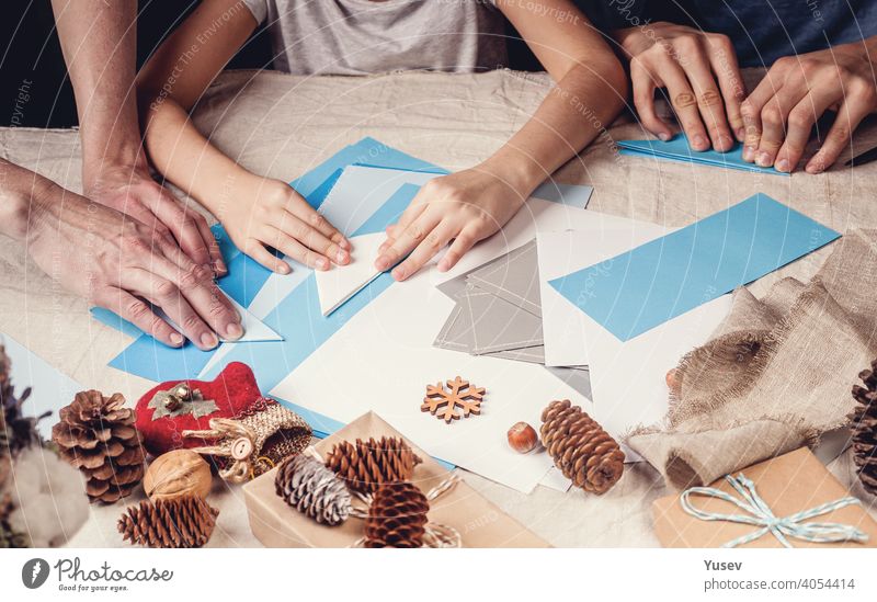 Hands of a caucasian mother and her daughter are cutting paper snowflakes with scissors. Handmade, christmas decorations, family winter activity. Close-up. Banner format