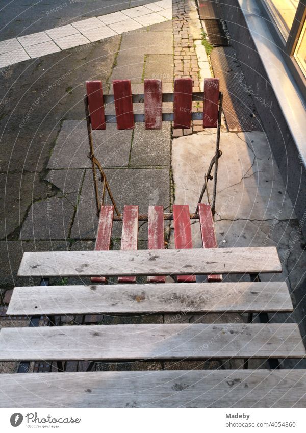 Bistro table with bistro chair on wildly mixed street pavement in artificial light in the evening in front of a shop window in the north end of Frankfurt am Main in Hesse