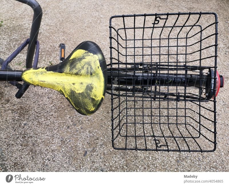 Black bicycle with bicycle basket and yellow painted bicycle saddle on natural coloured gravel in the Senckenberganlage in Frankfurt on the Main in Hesse