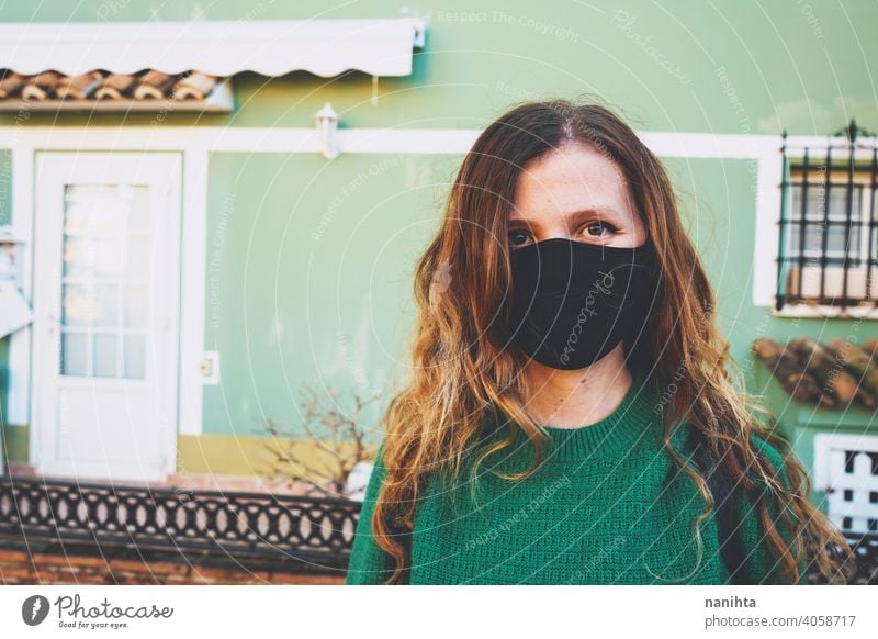 Young woman wearing a black face mask against an urban green wall coronavirus headshot casual life real real people colorful warm warmth lifestyle long hair