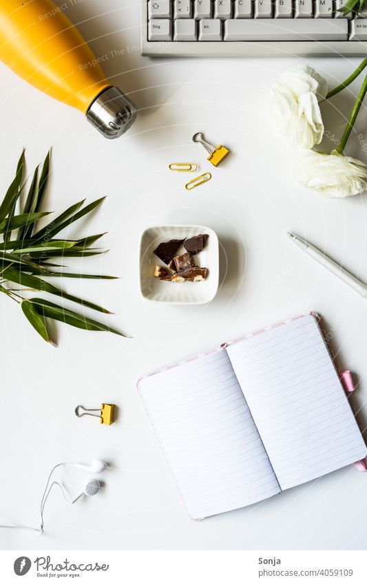 An empty notebook, a yellow water bottle, office supplies, and chocolate in a bowl. Notebook Empty Chocolate Bottle of water Desk Keyboard Office supplies