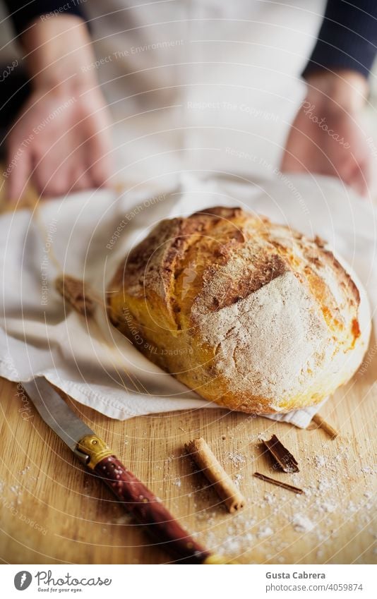 Artisan bread on a wooden board with a knife, pieces of cinnamon and a little flour, with a person out of focus in the background. baker bakery breakfast