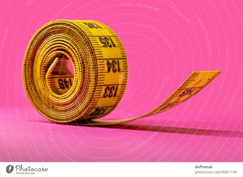 Macro shot of rolled up yellow tape measure on pink background Studio shot Studio lighting Pink Yellow Tape measure Coil meter tape Band Rollup Diet decrease