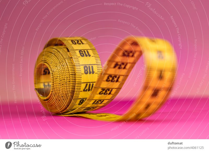 Macro shot of rolled up yellow tape measure on pink background Studio shot Studio lighting Pink Yellow Tape measure Coil meter tape Band Rollup Diet decrease