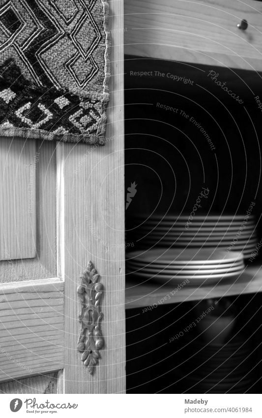 White plates on the shelf of an old farmer's cupboard made of solid wood in the living room of an old farmhouse in Rudersau near Rottenbuch in the district of Weilheim-Schongau in Upper Bavaria, photographed in neo-realistic black and white