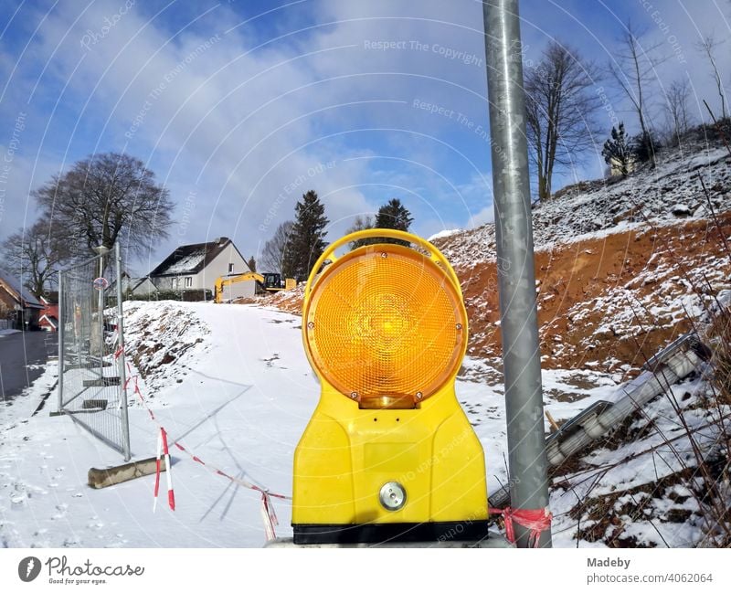 Gelb leuchtende Warnleuchte im Winter mit Schnee und Sonnenschein an einer Baustelle in Oerlinghausen bei Bielefeld am Hermannsweg im Teutoburger Wald in Ostwestfalen-Lippe