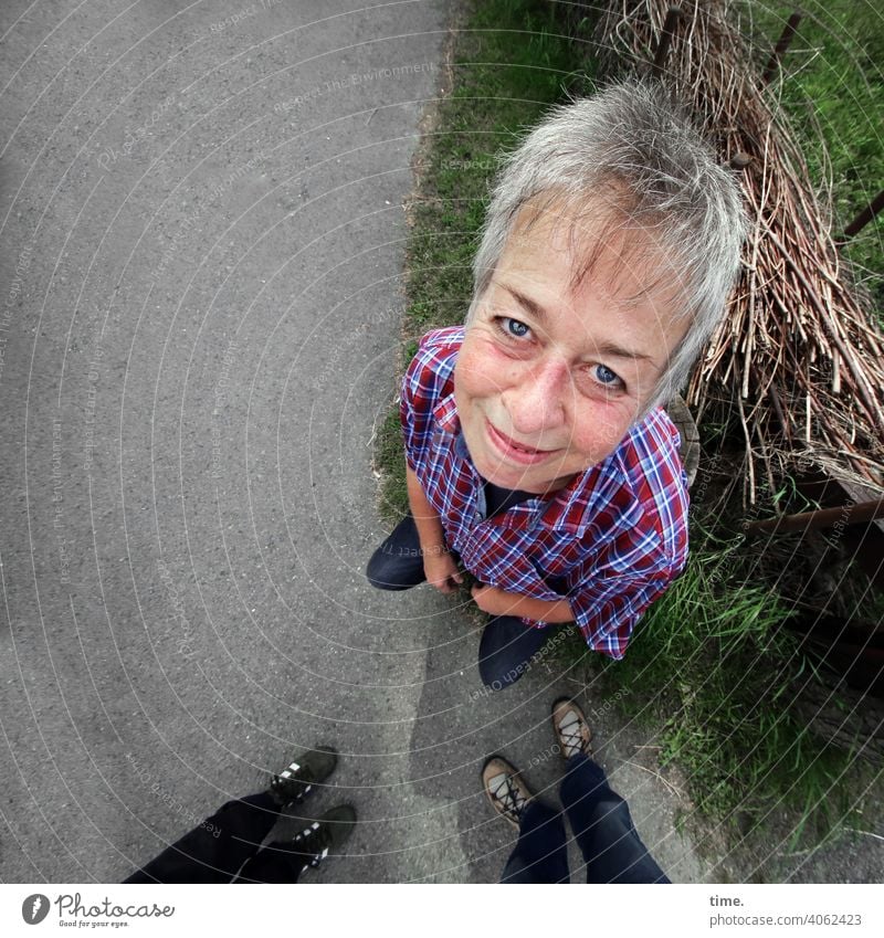 band of straw Woman Looking Perspective Bird's-eye view Street look Smiling Short-haired Blonde checkered shirt Meadow Straw feet kind Pleasant Asphalt