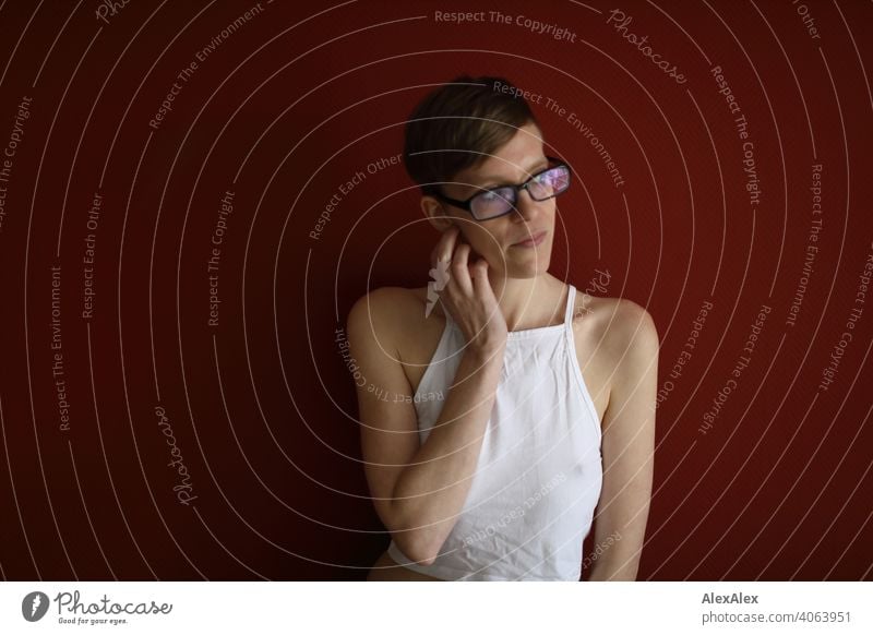 Young woman with top stands in front of red wall and looks out of window Woman Slim jeans Top Eyeglasses sits Shoulders Skin Large Athletic Articulated inside