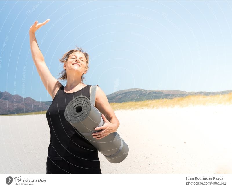 Woman in sportswear enjoying at the beach with a rolled-up mat under her arm energy fitness pilates active exercising training sunny outdoor vitality yoga mat