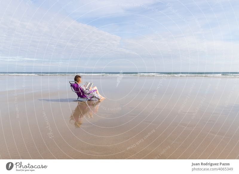 Woman reading a book sitting on a chair on a lonely beach sea outdoor social distance woman relax peaceful lifestyle vacation girl leisure female ocean shore