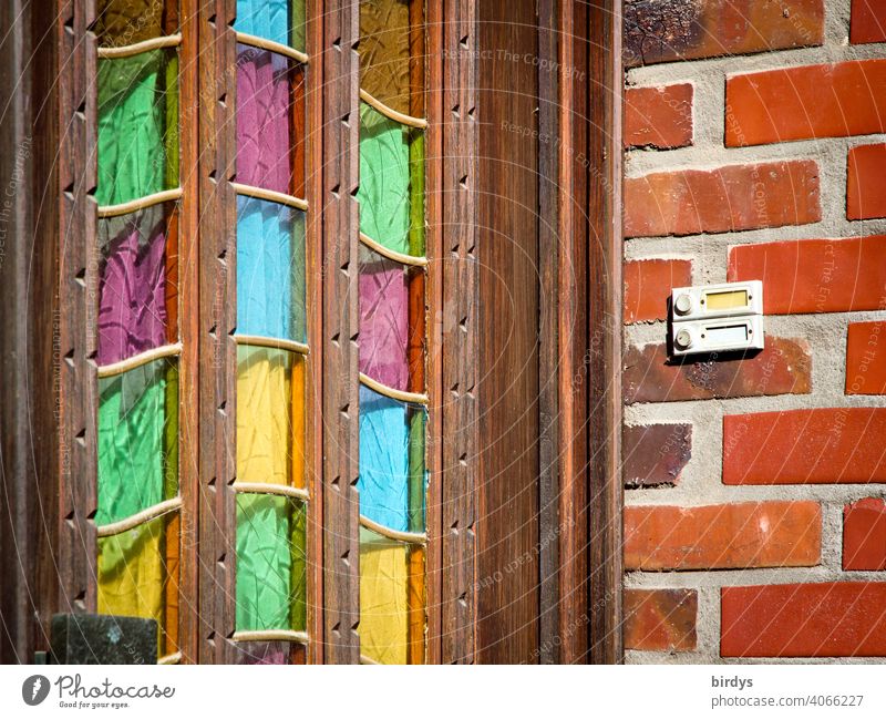 Old wooden house entrance door with coloured glass panes, brick wall with bell.entrance front door Entrance Wooden door Glass panes variegated Multicoloured