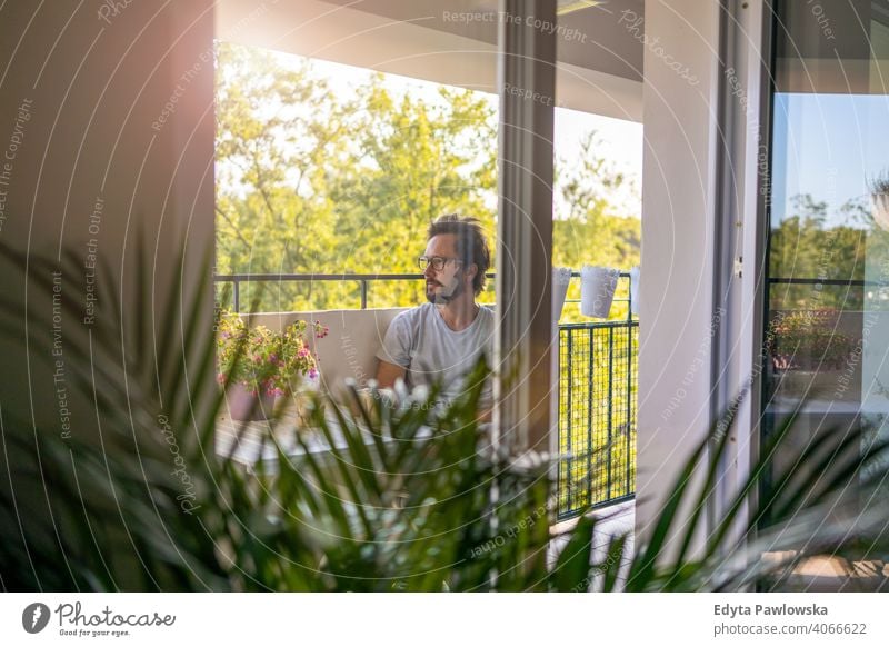 Man drinking coffee on the balcony of his apartment fresh air rest quarantine potted plant stay at home glasses lockdown simple life terrace healthy lifestyle