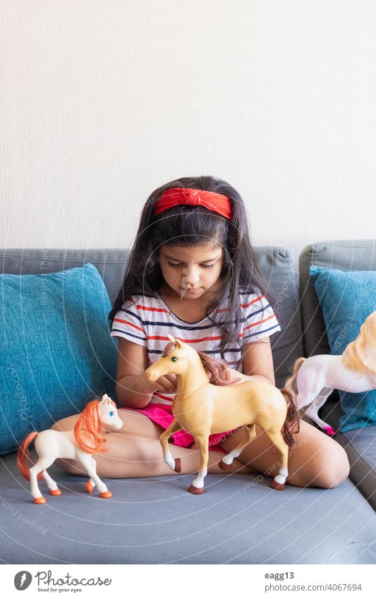 Little girl playing playing with her toy horses on the sofa alone apartment black hair carefree casual clothing child childhood color image comfortable