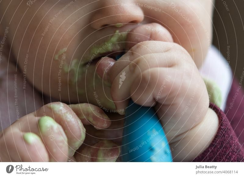 Close up of baby feeding self a green smoothie with spoon; messy baby led weaning first food baby food self feed infant child 6-12 months old smoothie bowl