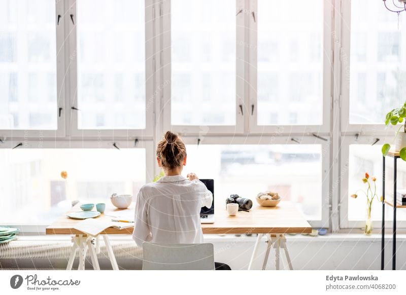 Rear view of young woman working on laptop in loft office millennials student hipster indoors window natural girl adult one attractive successful people