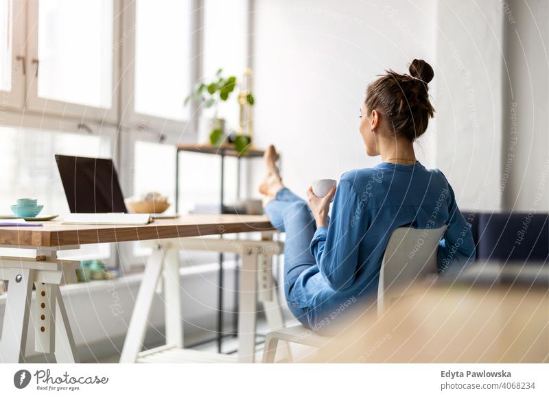 Young woman relaxing in office with her bare feet on desk millennials student hipster indoors loft window natural girl adult one attractive successful people