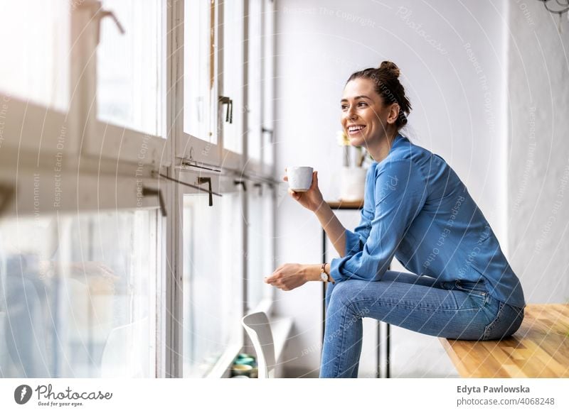 Young woman drinking coffee and looking out of a window millennials student hipster indoors loft natural girl adult one attractive successful people confident