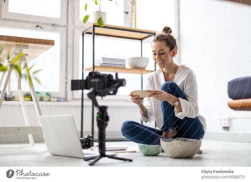 Female vlogger making social media video about her pottery laptop internet online computer technology shop retailer items workshop selling sitting floor