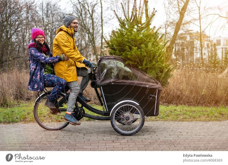 Couple having a ride with cargo bike transporting Christmas tree sustainable transport fun joy enjoying hipster modern carrying millennial winter ecologic