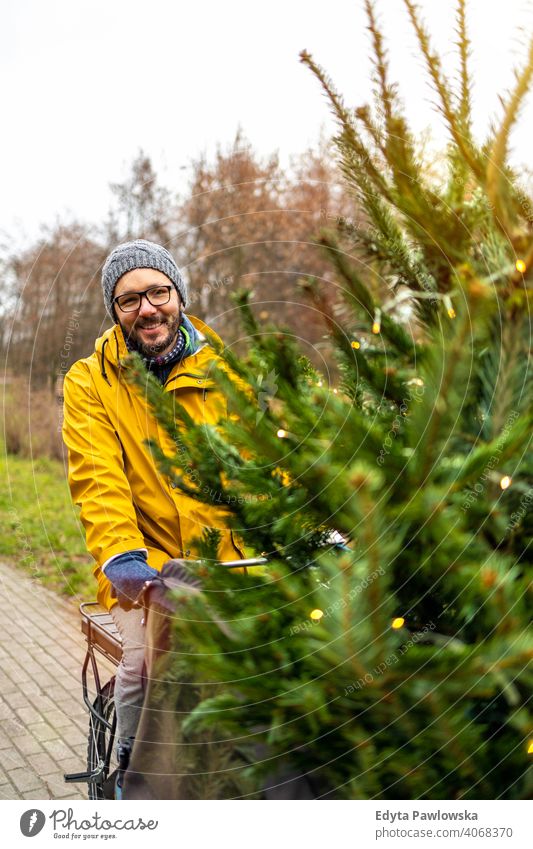 Man transporting Christmas tree on bicycle sustainable transport fun joy enjoying hipster modern carrying millennial winter ecologic ecology carbon footprint