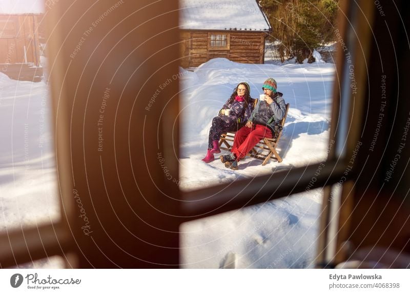 Couple enjoying winter day with cup of hot drink by wooden house couple through window window frame comfort chalet hygge cottage outside cabin rustic