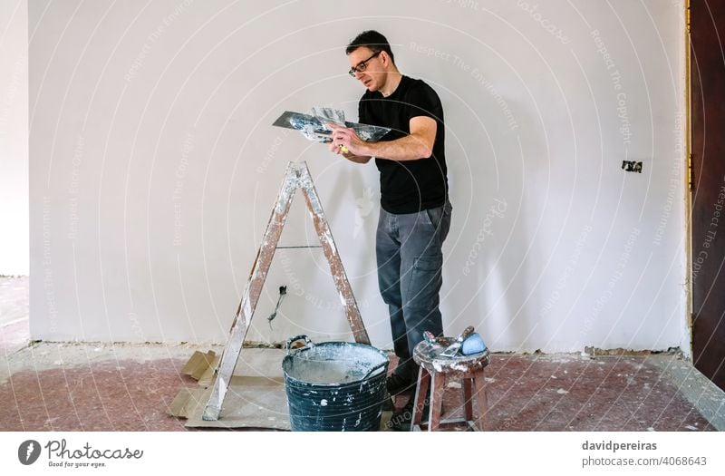 Builder working picking plaster with spatula builder plasterer picking up gypsum plaster trowel construction reform house stepladder bucket man worker person