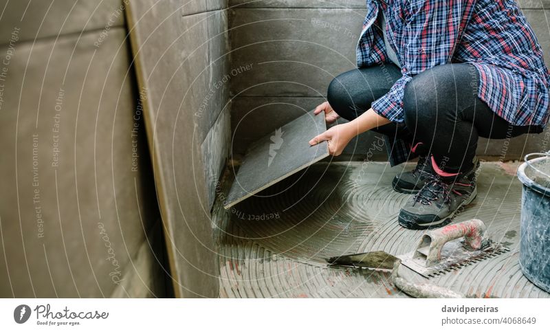 Female builder laying a new tile floor woman unrecognizable workman handyman placing tiling manual worker glazed terrace working construction mason tool