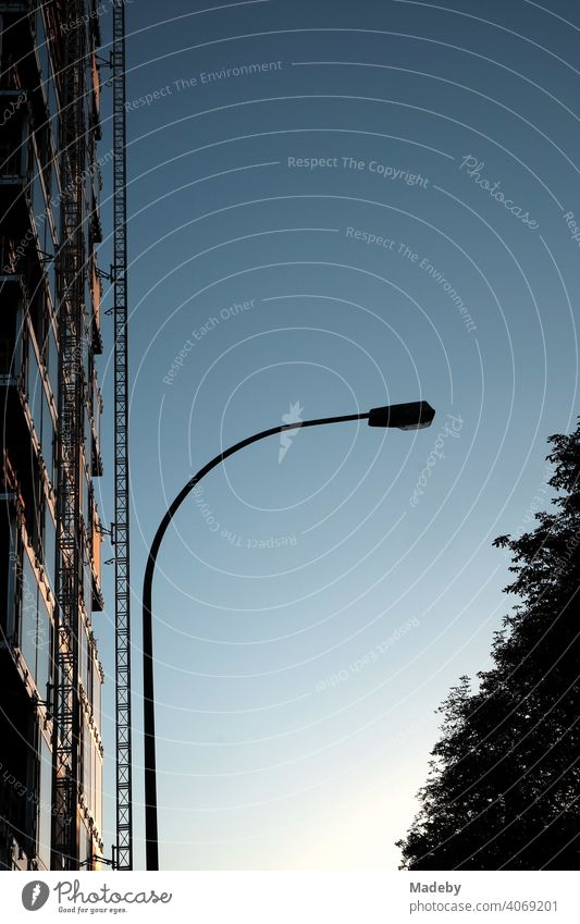 Curved streetlamp in front of a blue sky with the facade of a skyscraper with scaffolding in the light of the evening sun at Grüneburgpark in the Westend of Frankfurt am Main in Hesse, Germany