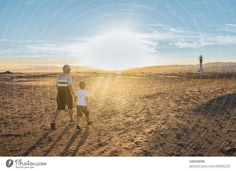 Grandfather and grandson hugging on a beach with a lighthouse in the background boy child childhood children coast dad day elderly family fangar far del fangar