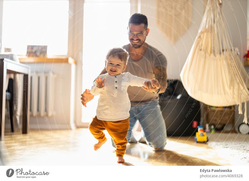 Little boy learning to walk with his father next to him at home single parent single dad fathers day fatherhood stay at home dad paternity leave modern manhood