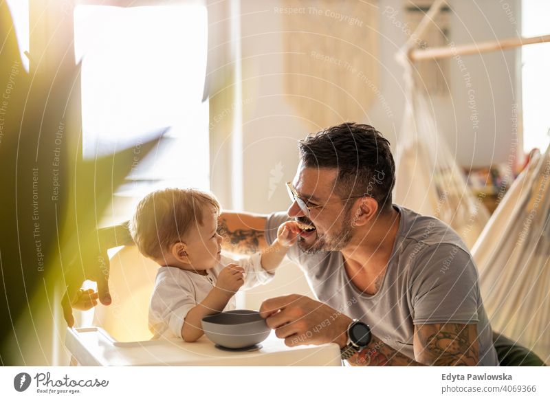 Single dad feeding his baby who is sat in a high chair single parent single dad fathers day fatherhood stay at home dad paternity leave modern manhood family