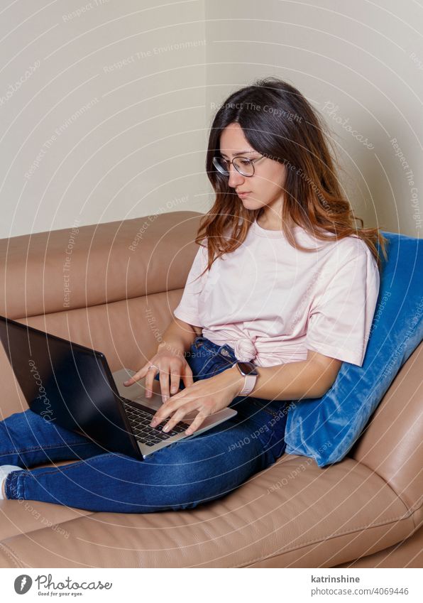 Young women using laptop while sitting on the sofa at home wear mockup t-shirt learn student Lifestyle jeans glasses serious concentrated indoor couch