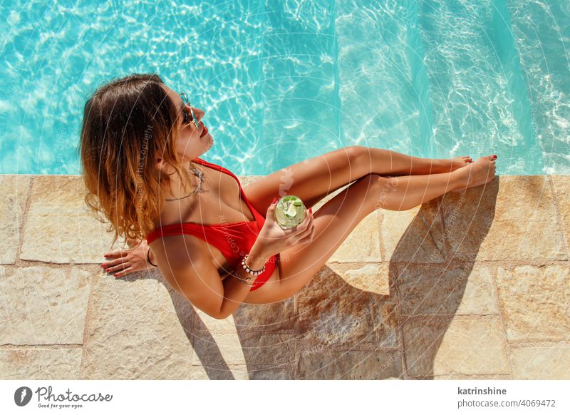 Young woman in red swimsuit with tropical cocktail mojito pool water one-piece Summer top view caucasian Fashion alone Happy smile Garden Emotion Outdoor Exotic