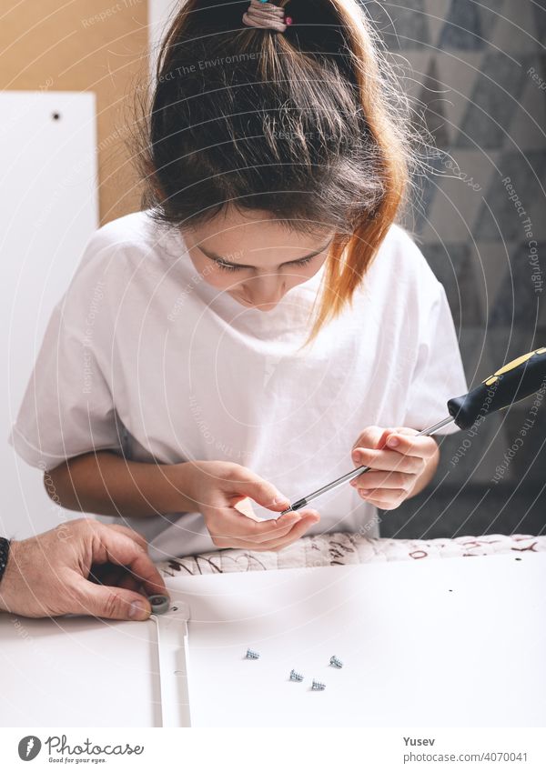 Little cute girl are holding a screwdriver and screws. Housework, furniture assembling. Vertical shot. little caucasian housework top view tool child repair