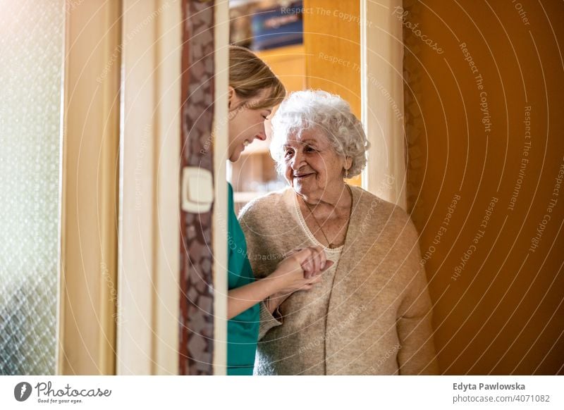 Friendly nurse supporting an elderly lady real people candid genuine woman senior mature female Caucasian home house old aging domestic life grandmother