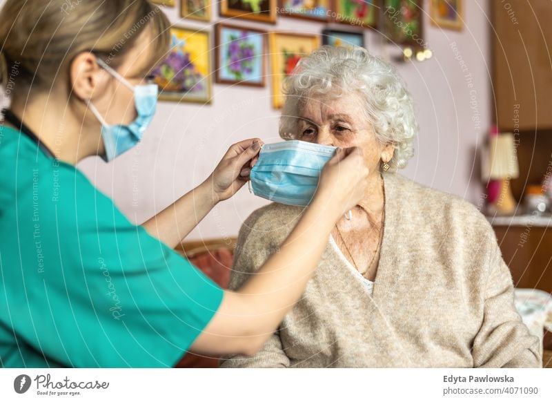 Female nurse helping a senior woman to put on protective face mask during home visit coronavirus real people covid elderly candid genuine mature female