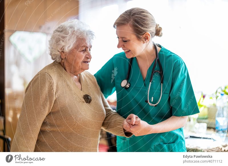 Friendly nurse supporting an elderly lady real people candid genuine woman senior mature female Caucasian home house old aging domestic life grandmother