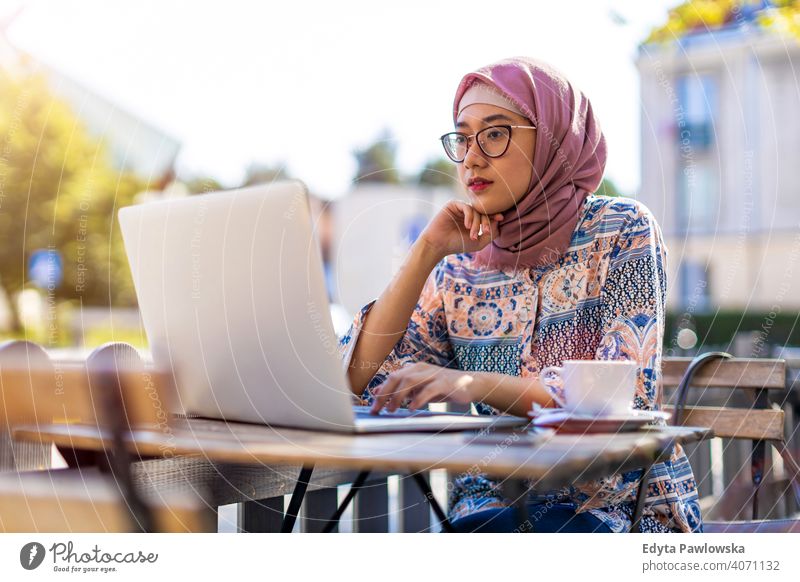 Young Muslim woman using a laptop in outdoor cafe hijab headscarf muslim islam arabic summer girl people young adult female lifestyle active outdoors millennial