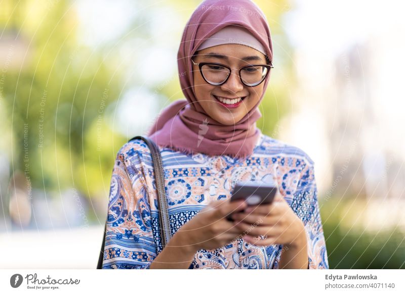 Smiling young muslim woman using mobile phone outdoors hijab headscarf islam arabic summer girl people young adult female lifestyle active millennial outside