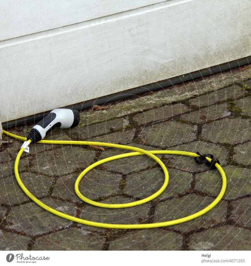 yellow charging cable with plug lies in front of a garage and waits for the electric car Cable charger cable Connector power supply Electricity Technology