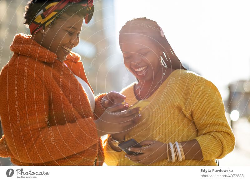 Happy female friends sending messages with their smartphones in the city diversity diverse people love outdoors day positivity confident carefree woman adult