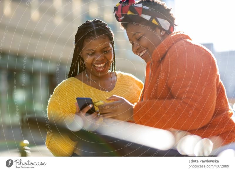 Happy female friends sending messages with their smartphones in the city diversity diverse people love outdoors day positivity confident carefree woman adult