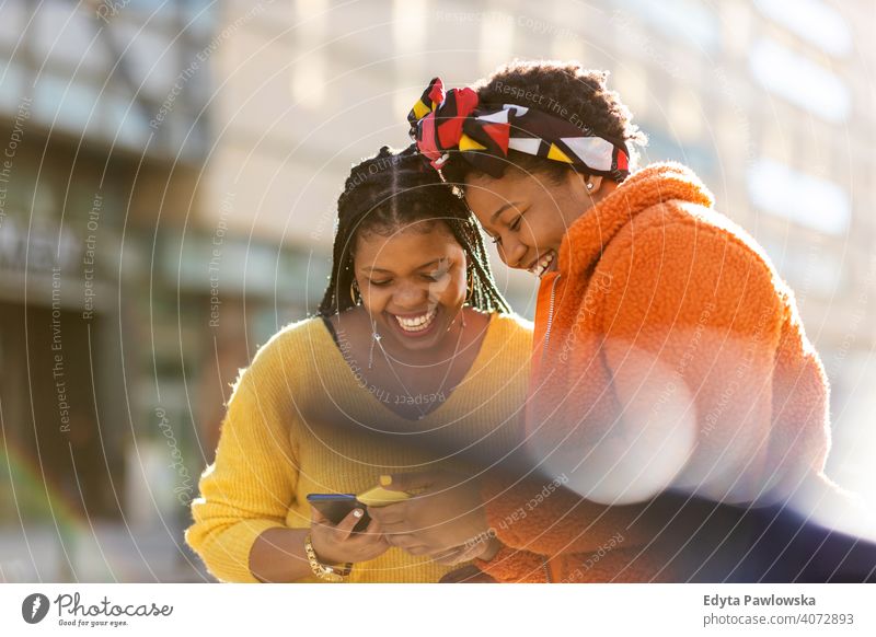 Happy female friends sending messages with their smartphones in the city diversity diverse people love outdoors day positivity confident carefree woman adult