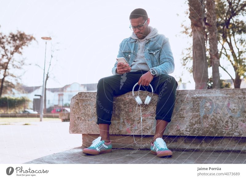 black boy sitting on a bench listening to music male earphones outdoors alone young 1 adult man smiling people technology path cheerful happiness closeup fun